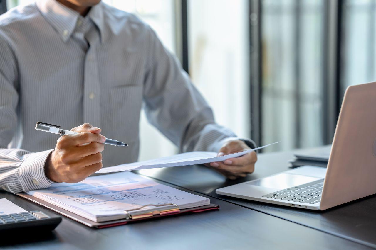 A business professional reviewing financial documents at a desk with a laptop
