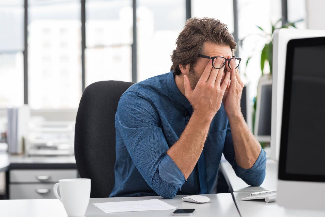 A stressed business director sitting at his desk with his head in his hands.