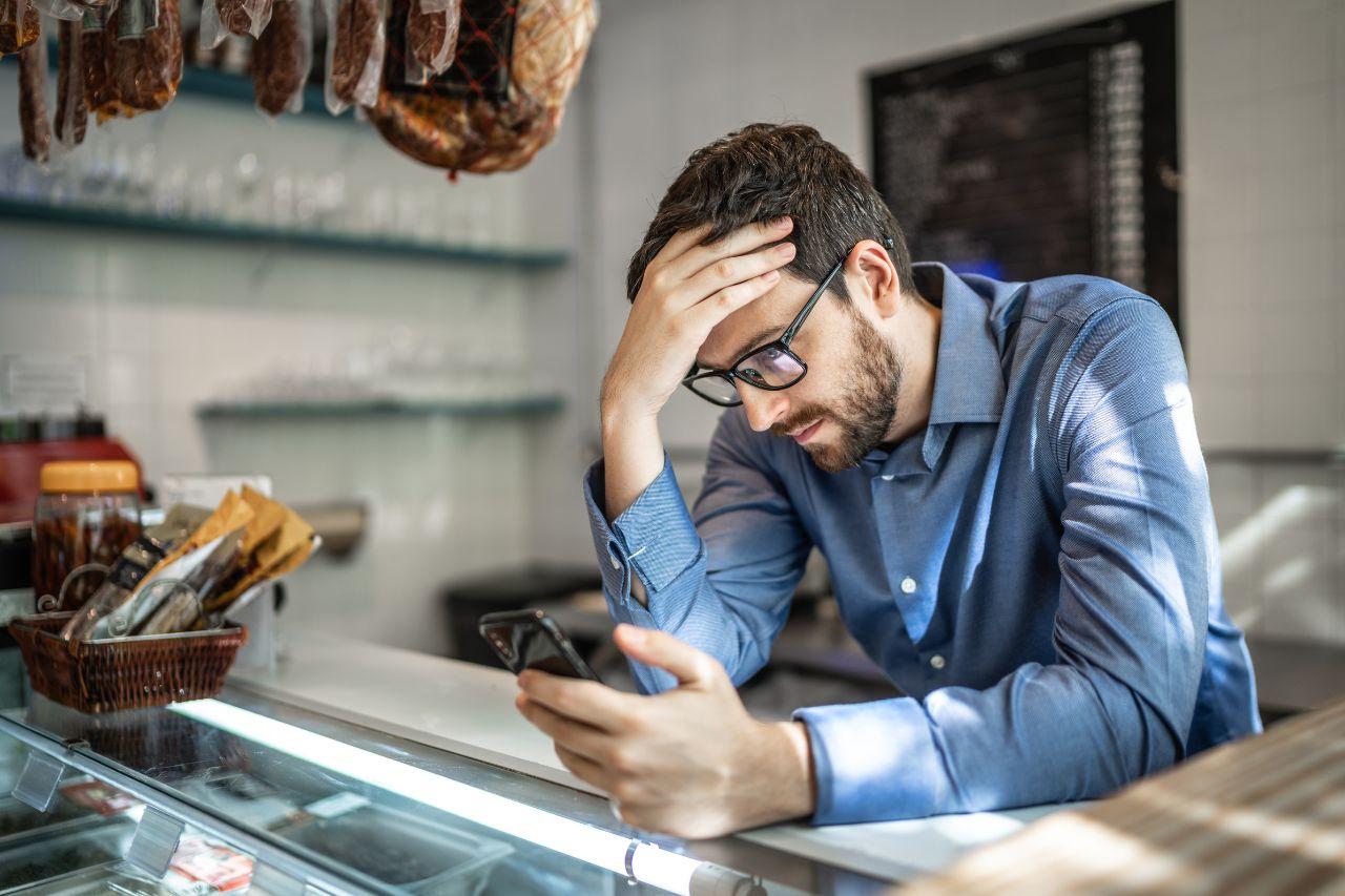 A stressed small business owner leaning on a counter looking at his phone with concern